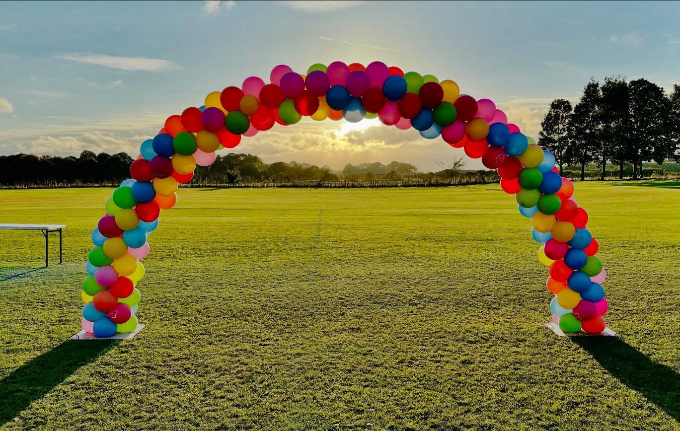 Rainbow balloon arch on a playing field at sunset